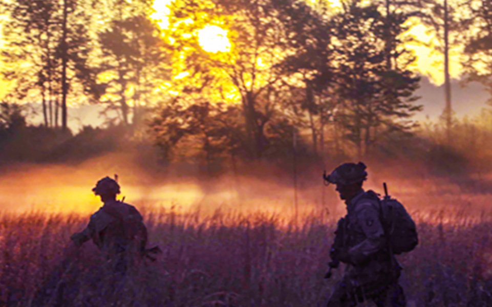 Two uniformed service members walking through a field in the early morning.