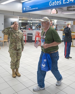 An Airmen dressed in camouflage salutes as a veteran walks by dress in a green honor flight shirt and blue jeans
