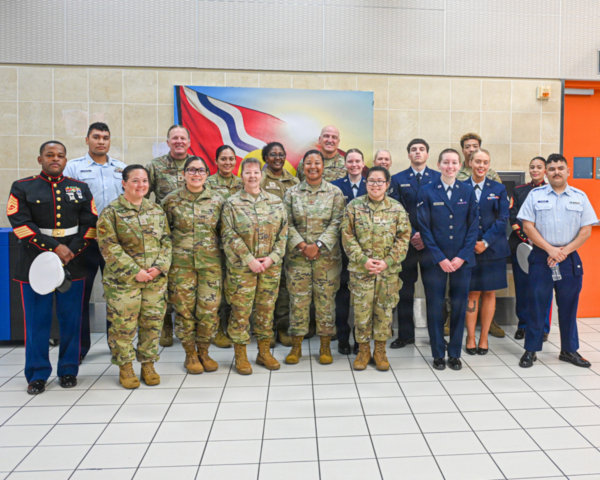 A group of servicemembers from the Marines, Coast Guard and Air Force stand in front of the flag of St. Louis in the Terminal at St. Louis Lambert International Airport.