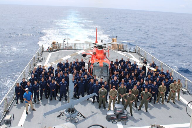 Crew members from Coast Guard Cutter Midgett (WMSL 757), the Coast Guard Helicopter Interdiction Tactical Squadron (HITRON), Coast Guard Tactical Law Enforcement Team – South personnel pose for a group photo aboard the Cutter Midgett's flight deck, alongside an unmanned ariel vehicle and an MH-65 Dolphin helicopter while underway in the Eastern Pacific Ocean, Aug. 28, 2025