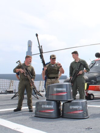 Coast Guard Helicopter Interdiction Tactical Squadron (HITRON) aircrew personnel aboard Coast Guard Cutter Midgett (WMSL 757) stand on the flight deck, displaying airborne use of force weapons from behind three bullet-damaged outboard engine cowlings in the Eastern Pacific Ocean.