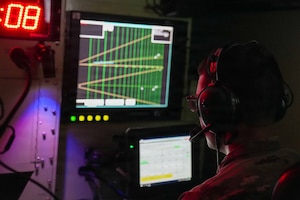 A person wearing a headset sits in a dark room while observing air traffic control monitoring equipment.