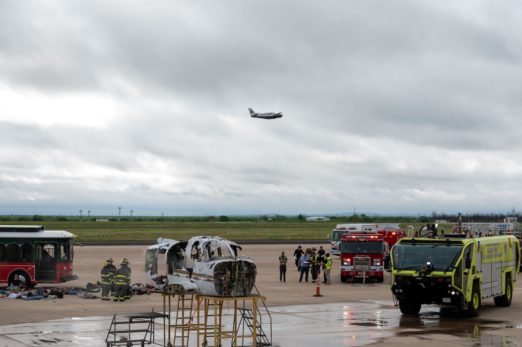 Emergency responders operate at the scene of a simulated mass casualty incident as an aircraft flies overhead during a joint emergency response exercise at Mathis Field, San Angelo Regional Airport, San Angelo, Texas, April 15, 2026.  The exercise integrated air and ground response elements. (U.S. Air Force photo by Senior Airman James Salellas)