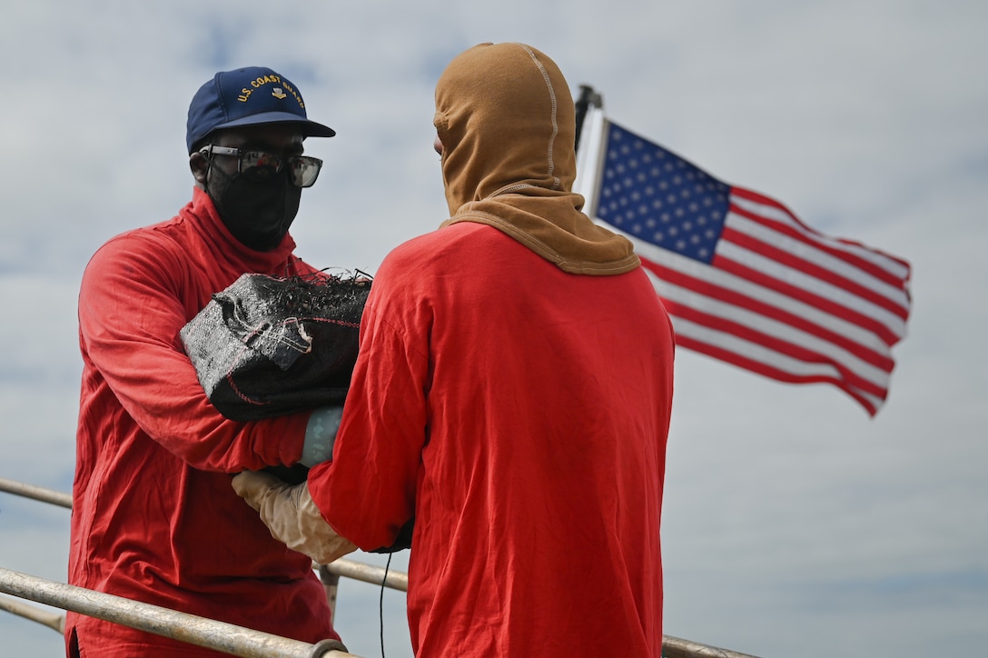 Two Coast Guard Cutter Tampa crewmembers pass a bale of cocaine during a drug offload at Base Miami Beach, Miami, Florida, April 16, 2026. The seized contraband was the result of two interdictions in international waters of the Eastern Pacific Ocean through Operation Pacific Viper, weighing approximately 3,825 pounds, and worth an estimated $28.7 million. (U.S. Coast Guard photo by Petty Officer 3rd Class Reese Hindmarsh)