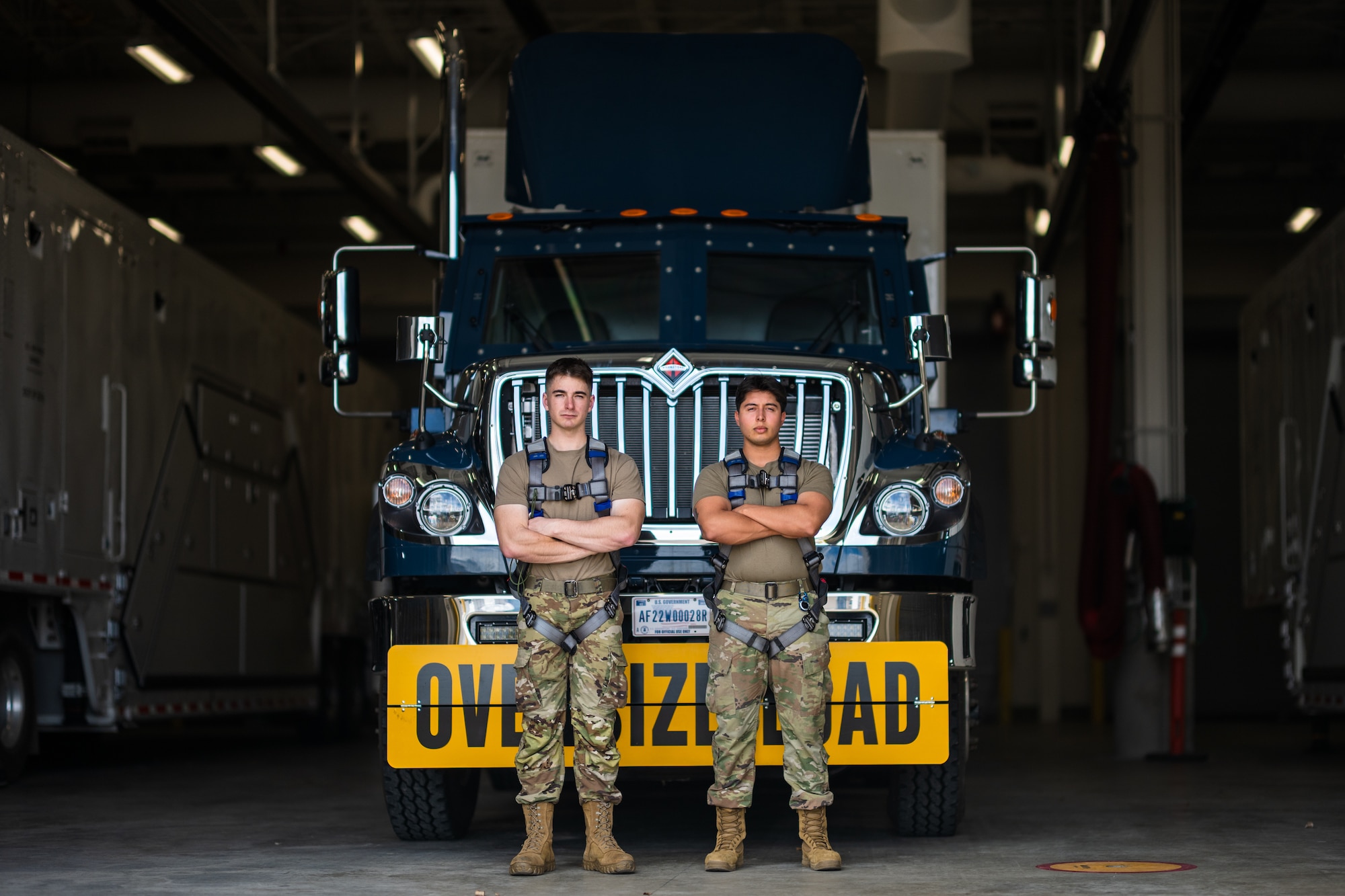 Two airmen stand in front of a payload transporter replacement.