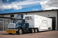 A payload transporter replacement is parked in front of a building