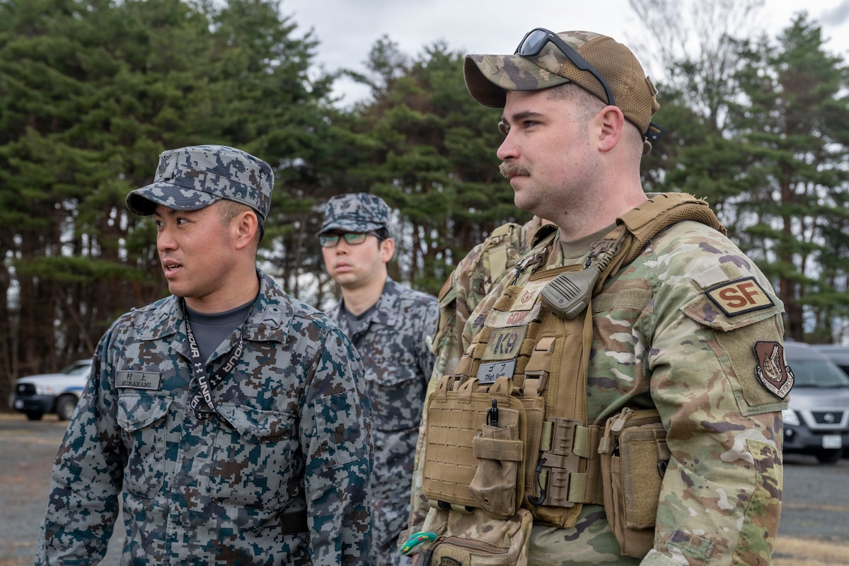 Japan Air Self-Defense Force (JASDF) Staff Sgt. Masaki Murakami, left, 3rd Air Wing security forces K-9 handler, JASDF Tech. Sgt. Daiki Saito, security forces K-9 handler, and U.S. Air Force Tech. Sgt. Steven Goff, 35th Security Forces Squadron military working dog handler, listen to a training scenario brief during a joint bilateral K-9 exercise at Misawa Air Base, Japan, April 7, 2026