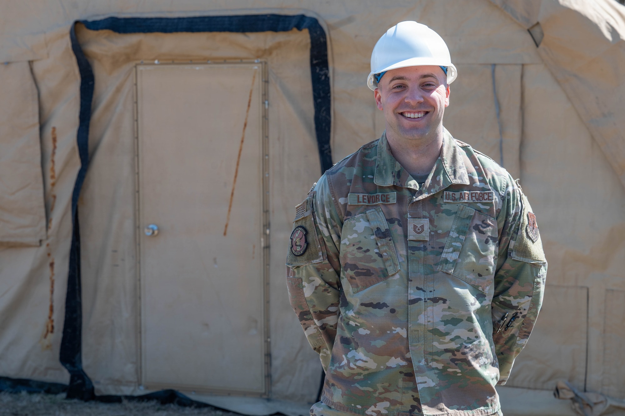An airman stands in front of a tent.