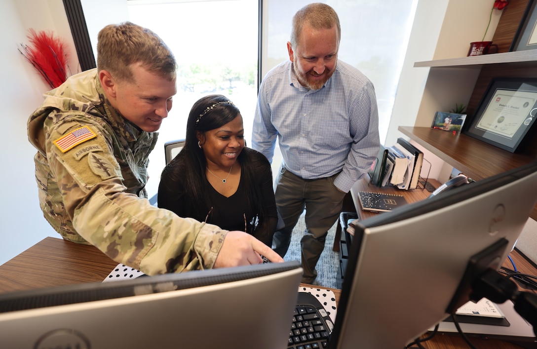 Woman sitting looking at a computer screen with two men looking on.