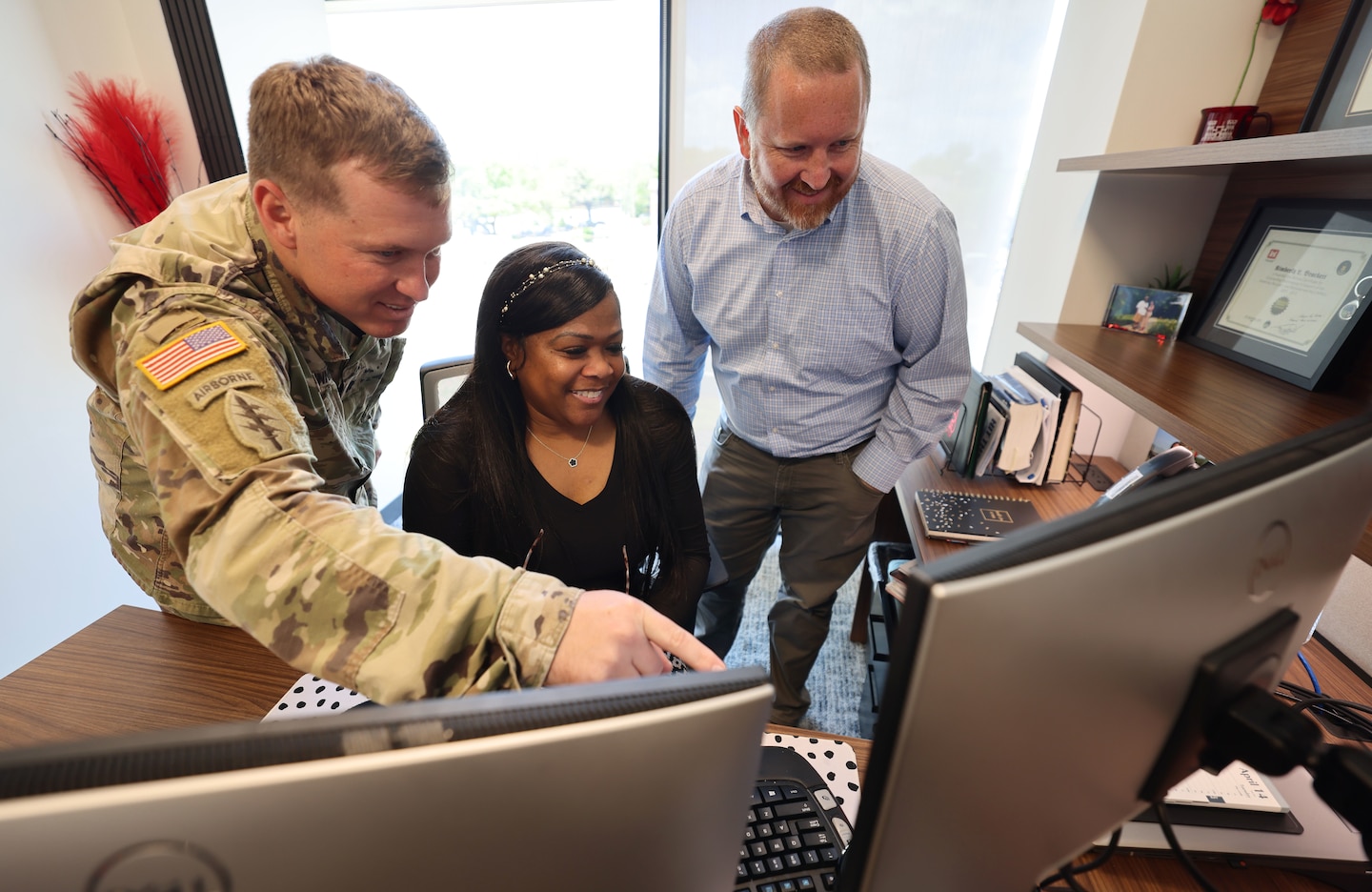 Woman sitting looking at a computer screen with two men looking on.