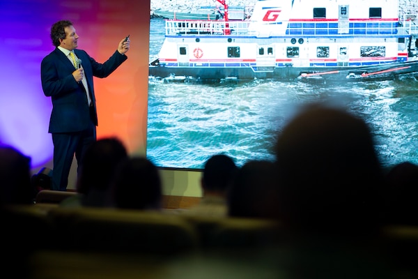 A man standing on a stage giving a presentation to people seated in an auditorium.