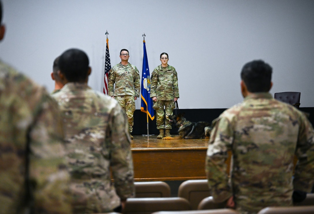 U.S. Air Force Maj. Joseph Ritchie, 316th Security Support Squadron commander, and Senior Airman Daylynn Robinson, 316th SSPTS military working dog handler, and Military Working Dog Baily, assigned to the 316th SSPTS, listen to the reading of the Air and Space Commendation Medal.