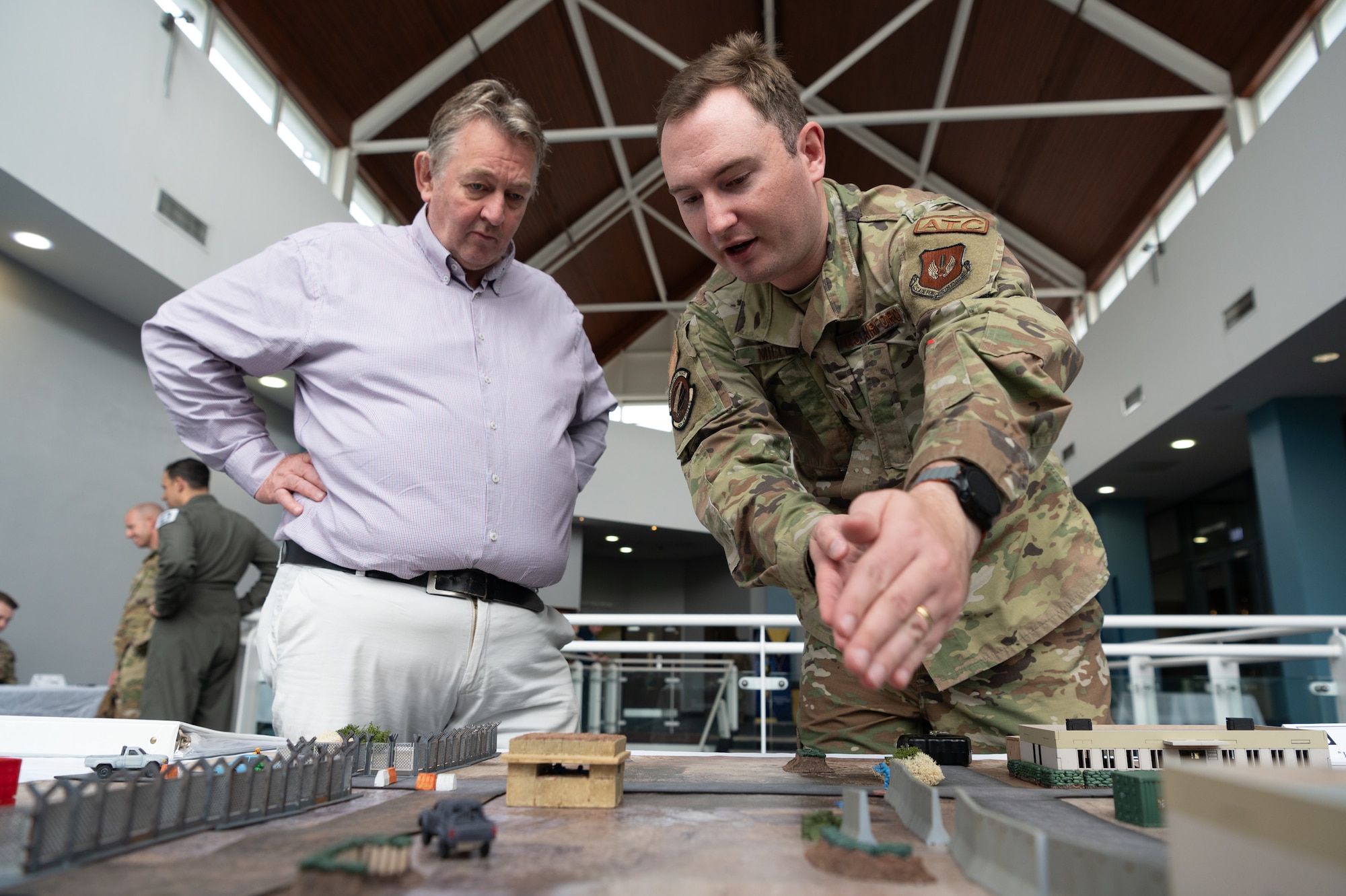 U.S. Air Force Tech. Sgt. Robert Miller, right, 420th Air Base Squadron air traffic control watch supervisor, teaches Nick Underwood, 501st Combat Support Wing process manager, about an integrated defense tabletop training during the Royal Spark Innovation Summit