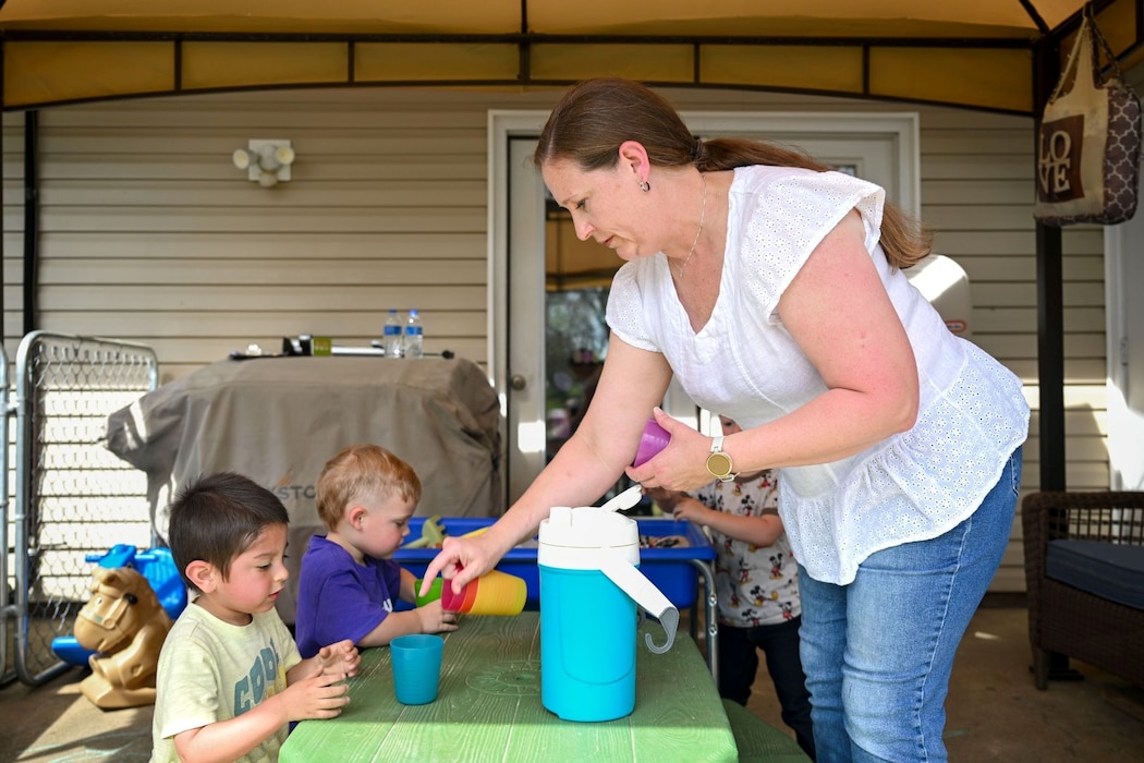A woman interacts and serves drinks to two small children.