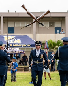 An Airman walks under two rifles thrown over his head.