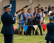 Students cheer outside while a drill team member performs in the foreground.