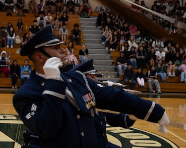 An Airman throws his rifle while performing in a gymnasium for students.