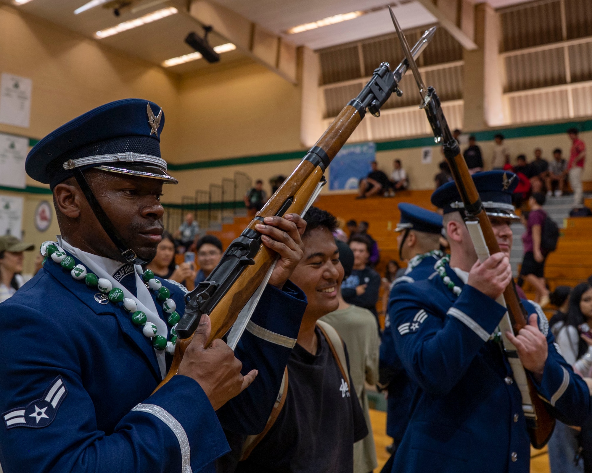A student poses with two Airmen holding rifles.