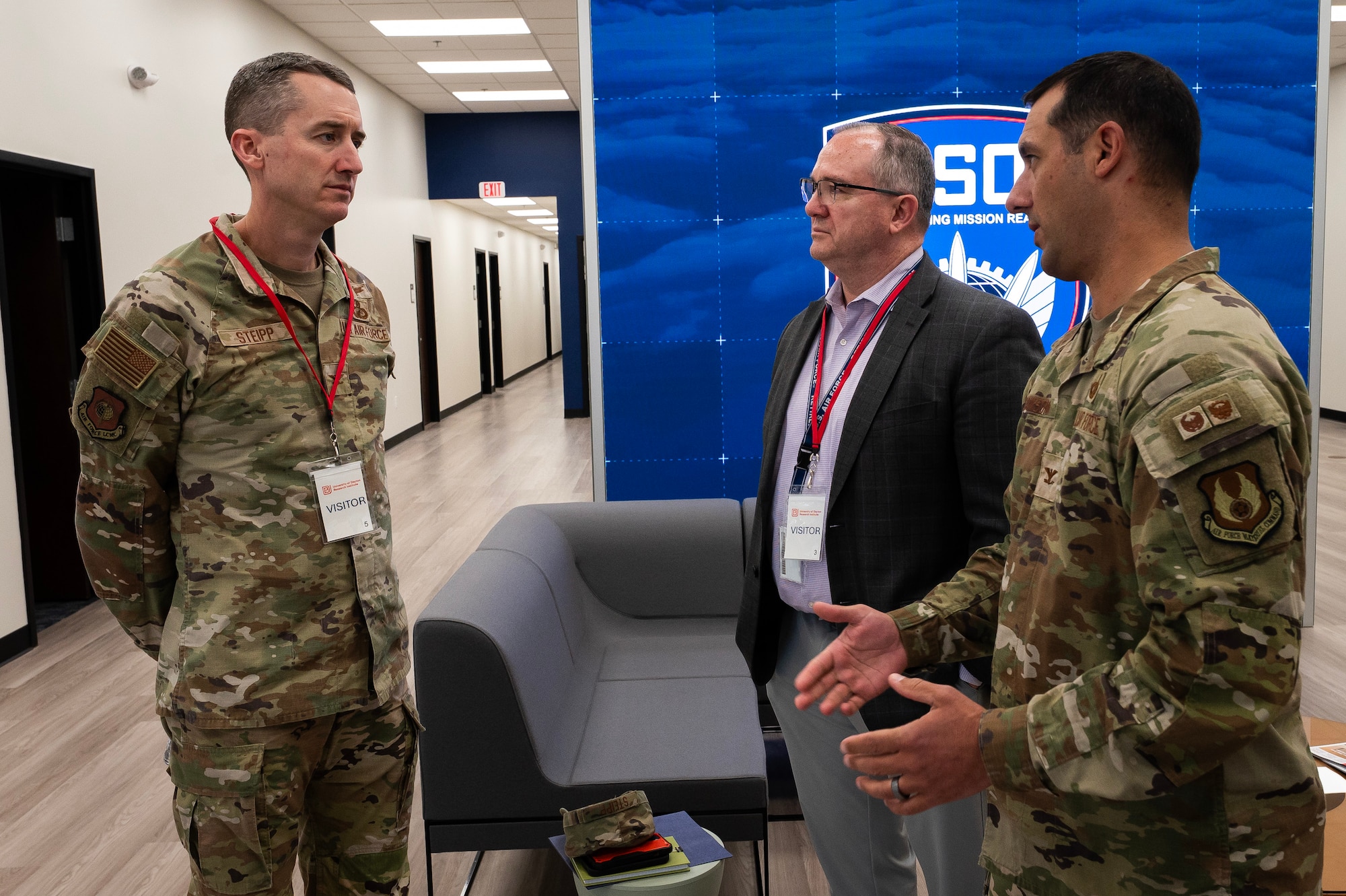 Two men in Air Force camo talk with man in suit jacket.