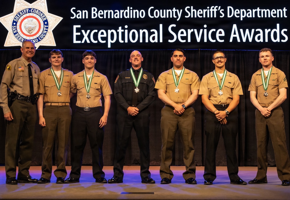U.S. Marine Corps Cpl. Fabian Navarro, third from right, Cpl. Hunter Richard, second from left, Cpl. Walker Swithenbank, first from right, and Cpl. Martin Tripp, unable to attend, U.S. Navy Hospitalman Apprentice Guilherme Crain, second from right, and Hospitalman Apprentice Luke Rowley, third from left, alongside Officer Brian Derby, middle, receive the Life Saving Award from the San Bernardino County Sheriff’s Department Exceptional Service Awards Ceremony from Sheriff Shannon Dicus, first from left, at Immanuel Baptist Church, Highland, California, April 9, 2026. On August 24, 2025, SB County Fire Department requested assistance in Johnson Valley after a dirt bike crash left a rider critically injured, six service members and a military police officer located the patient, provided first aid, and established communication. The rider was airlifted to a hospital, where staff credited the team with saving the rider’s life. (U.S. Marine Corps photo by Lance Cpl Karol Huizar)