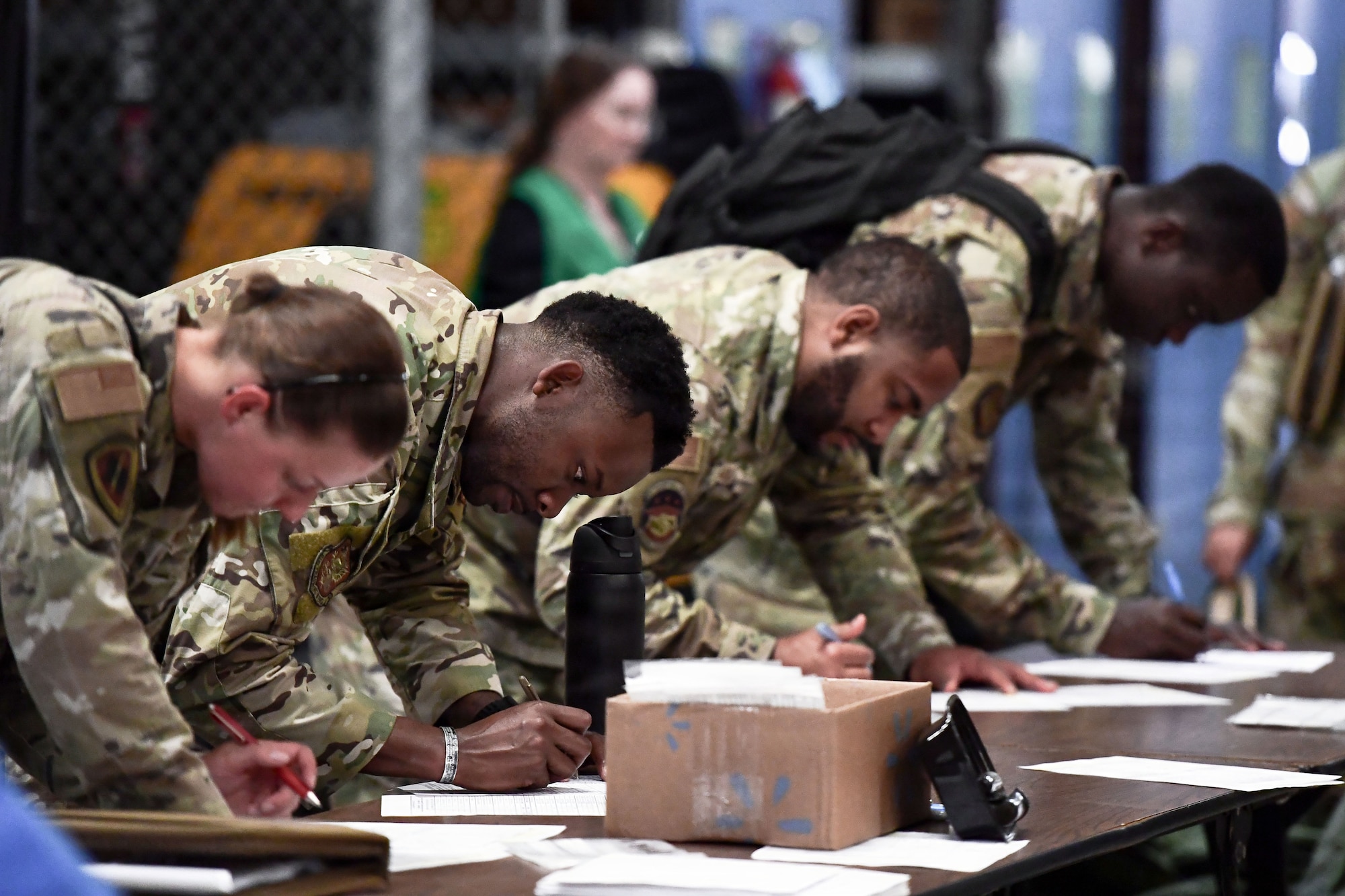 a medium shot of uniformed military members show them leaning on a table filling out paperwork at a table
