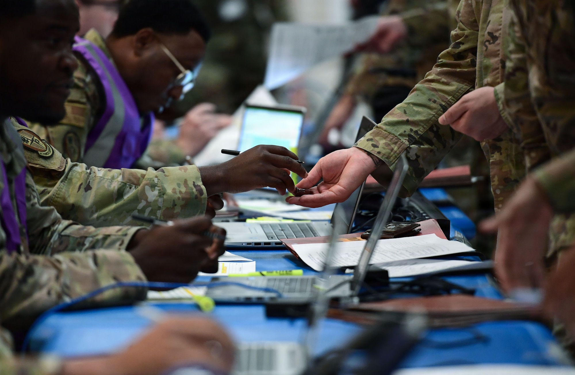 a close up show shows many sets of hands passing paperwork and dog tags during a deployment line