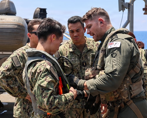 Royal Australian Navy (RAN) Leading Seaman Dominic Turkalj, assigned to RAN Anzac-class frigate HMAS Toowoomba (FFH 156), prepares U.S. Navy Lt. j.g. Nicholas Traylor, assigned to Whidbey Island-class dock landing ship USS Ashland (LSD 48), to embark Toowoomba’s MH-60R Sea Hawk for a crew exchange during a multilateral exercise with RAN and Royal Canadian Armed Forces in the South China Sea, April 14, 2026.