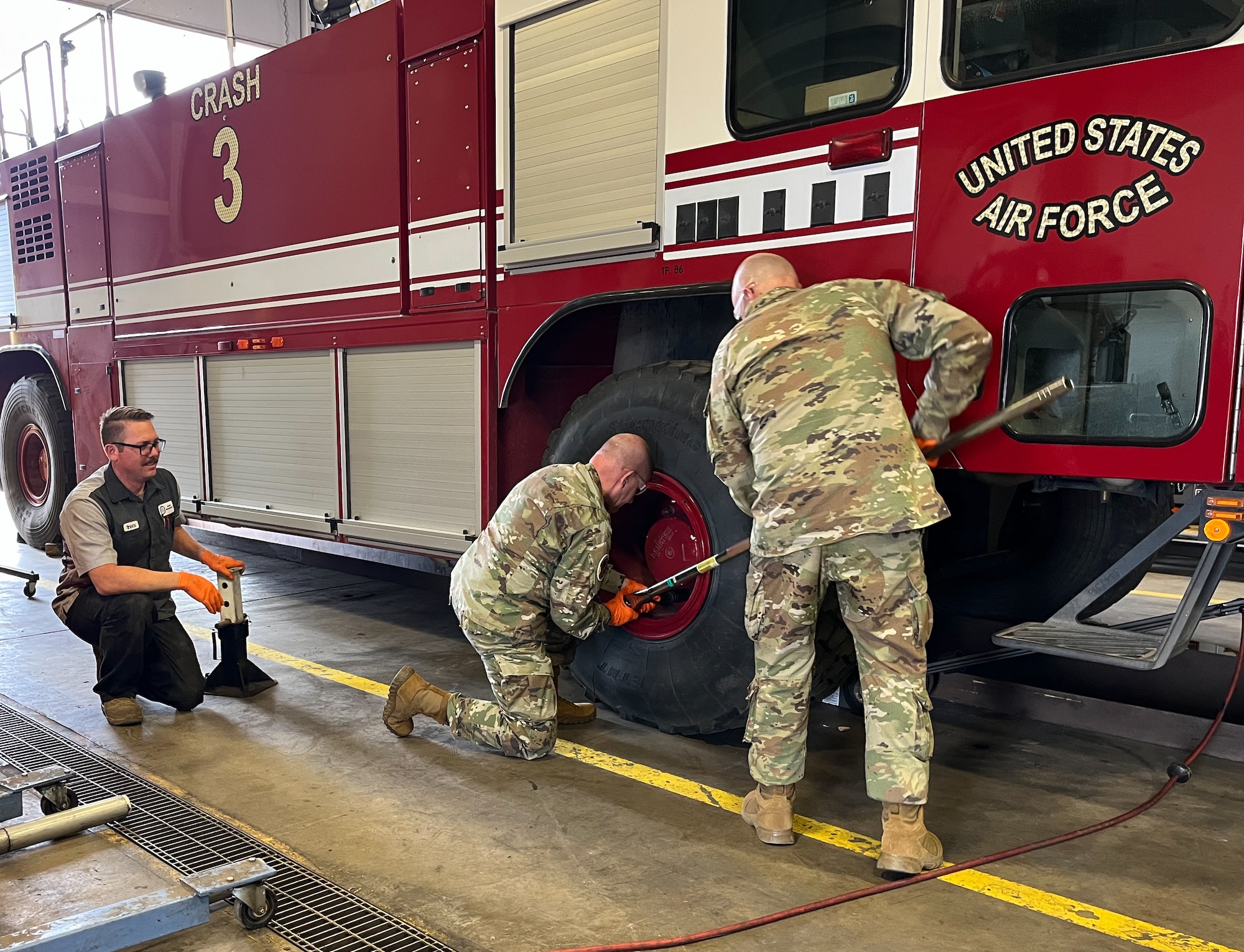 Col. Klock and Chief Master Sgt. Joslin service a tire on a firetruck while Tech. Sgt. Brooks looks on nearby.