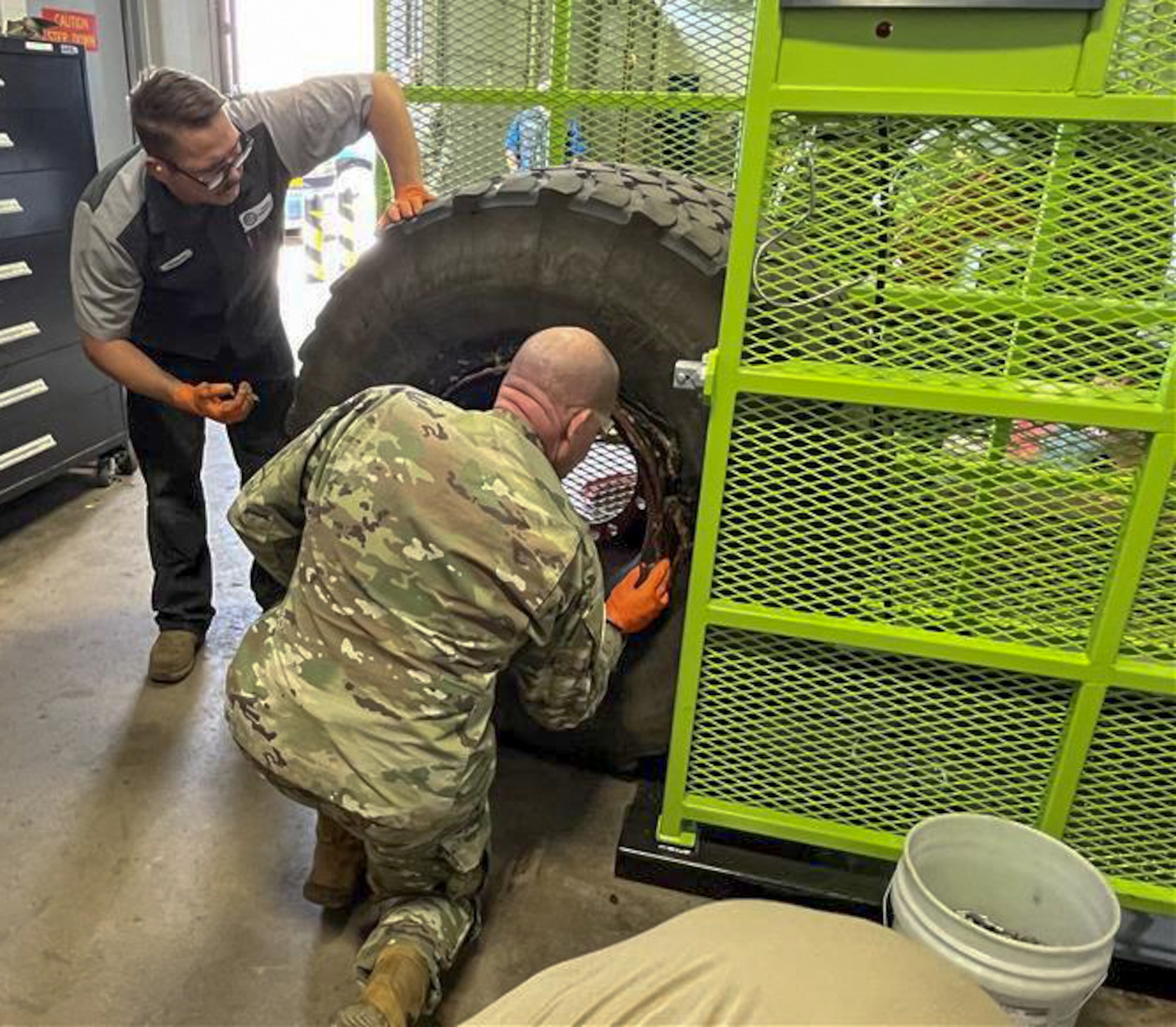 Col. Klock knees next to a tire while servicing it with Tech. Sgt. Brooks looking over the tire.