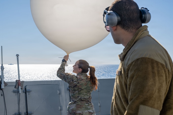 Air Force Senior Airman Tiffany Ziarnick, assigned to the 45th Weather Squadron, prepares to launch a weather balloon from the portside bridge wing of amphibious transport dock ship USS John P. Murtha (LPD 26), Jan. 26, 2026.