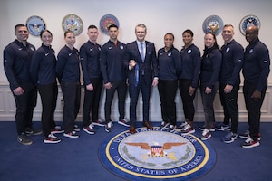 Nearly a dozen people in athletic attire pose for a group photo with a man in business attire in the center.