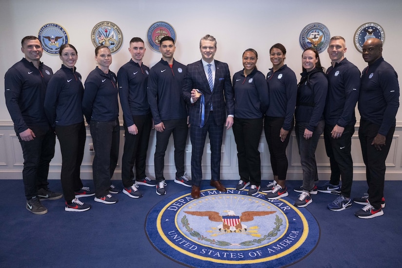 Nearly a dozen people in athletic attire pose for a group photo with a man in business attire in the center.