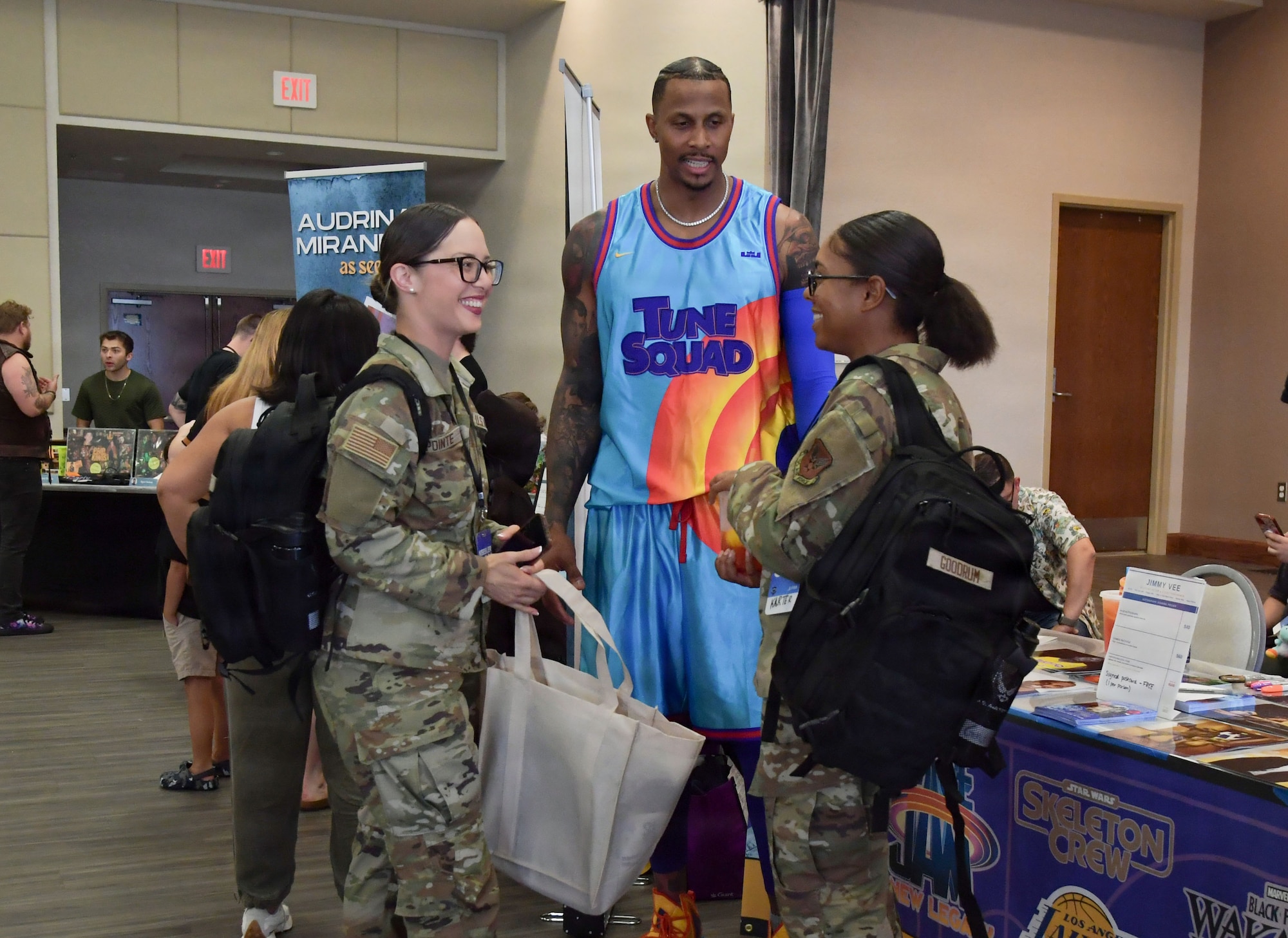 Two women wearing military uniform speaks with a gentleman wearing a colorful basketball uniform.