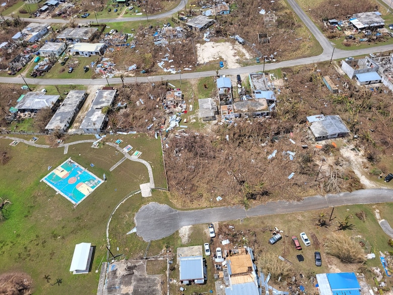 An aerial view of a community which has houses with no roof and debris is scattered along the landscape.