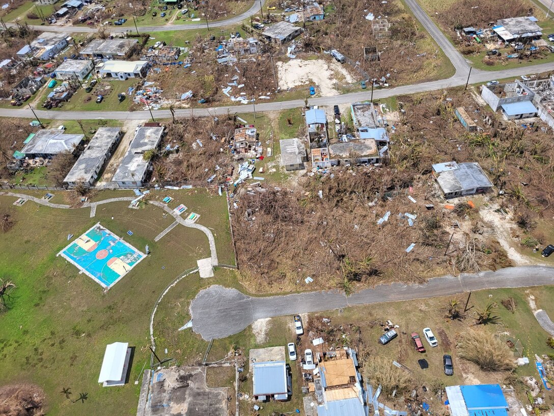 An aerial view of a community which has houses with no roof and debris is scattered along the landscape.