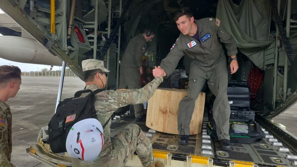 An aircrew member grabs the hand of a Soldier as he assists the Soldier up on to the back of a military cargo plane.