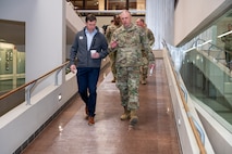 Two men, one in uniform, walking down a large indoor ramp. A group of men in uniform walk behind.
