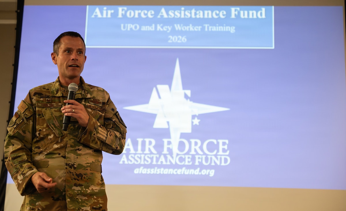 An Airman holding a microphone stands on a stage and gives a speech