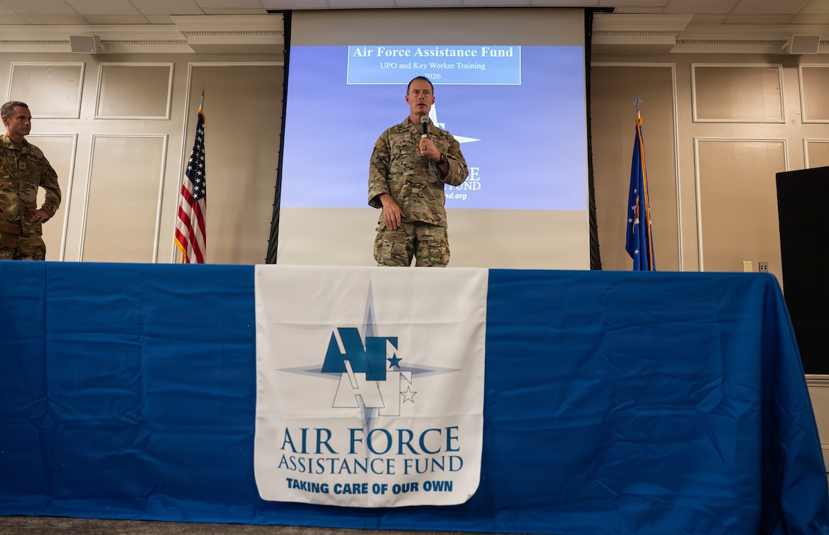An Airman holding a microphone stands on a stage and gives a speech