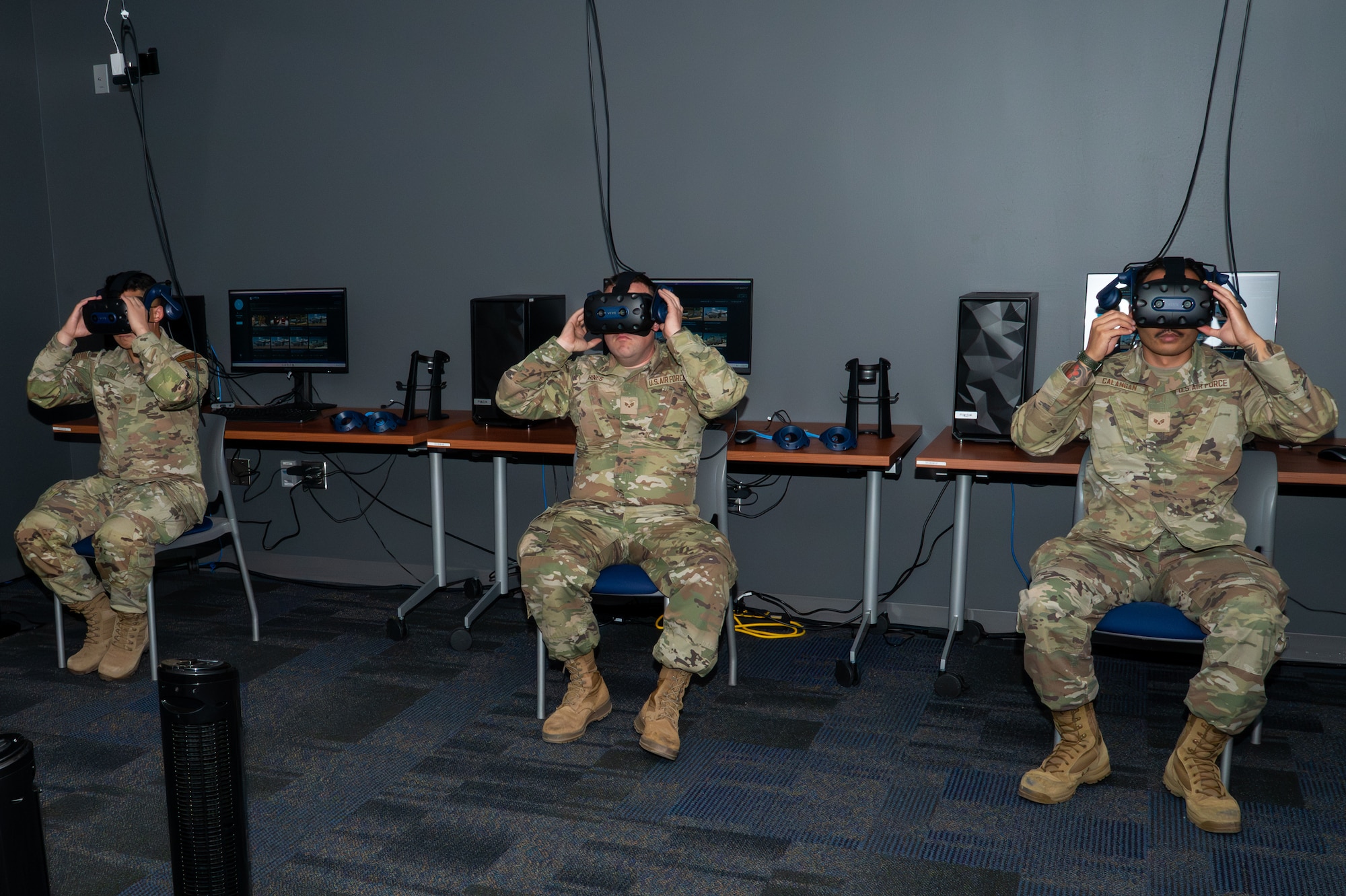 3 military members sitting in chairs putting on VR headsets.