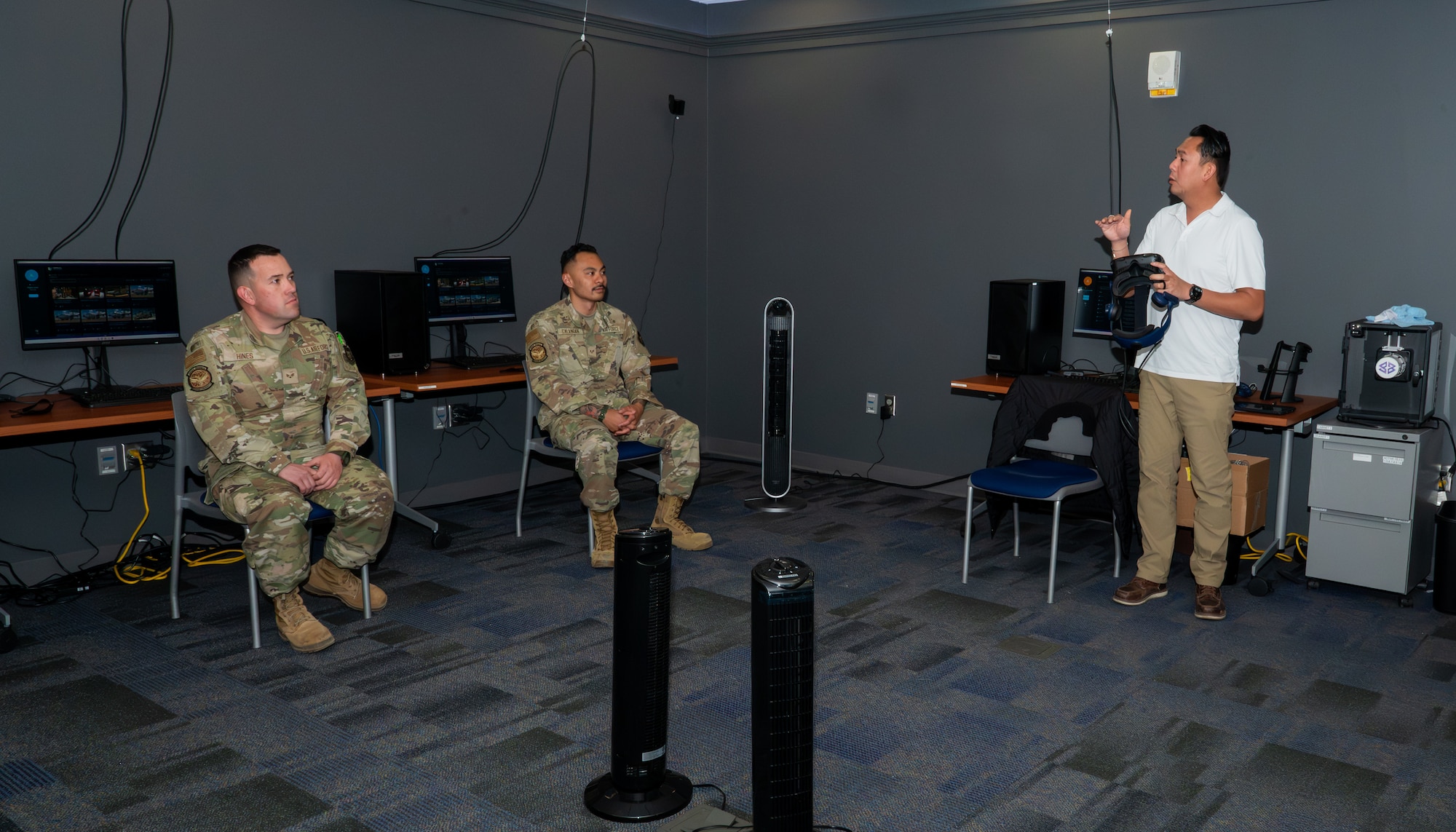 two military members sitting in chairs being instructed by an instructor on the vr system
