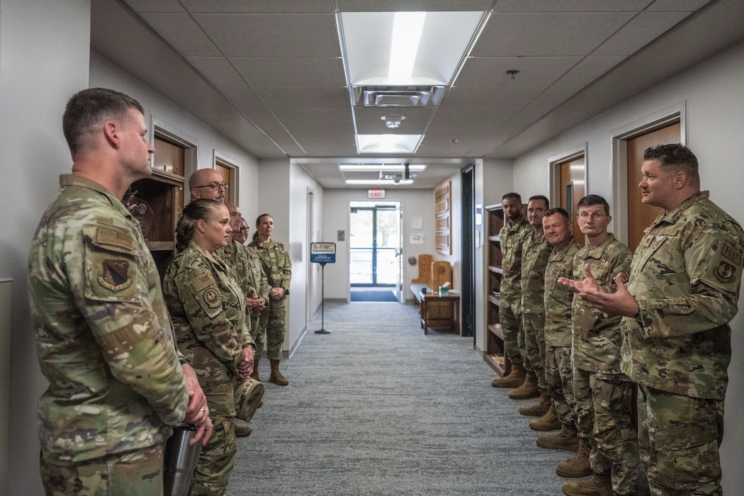 Airmen stand in a hallway while chaplain corps members brief a senior leader during a visit to a newly opened facility.