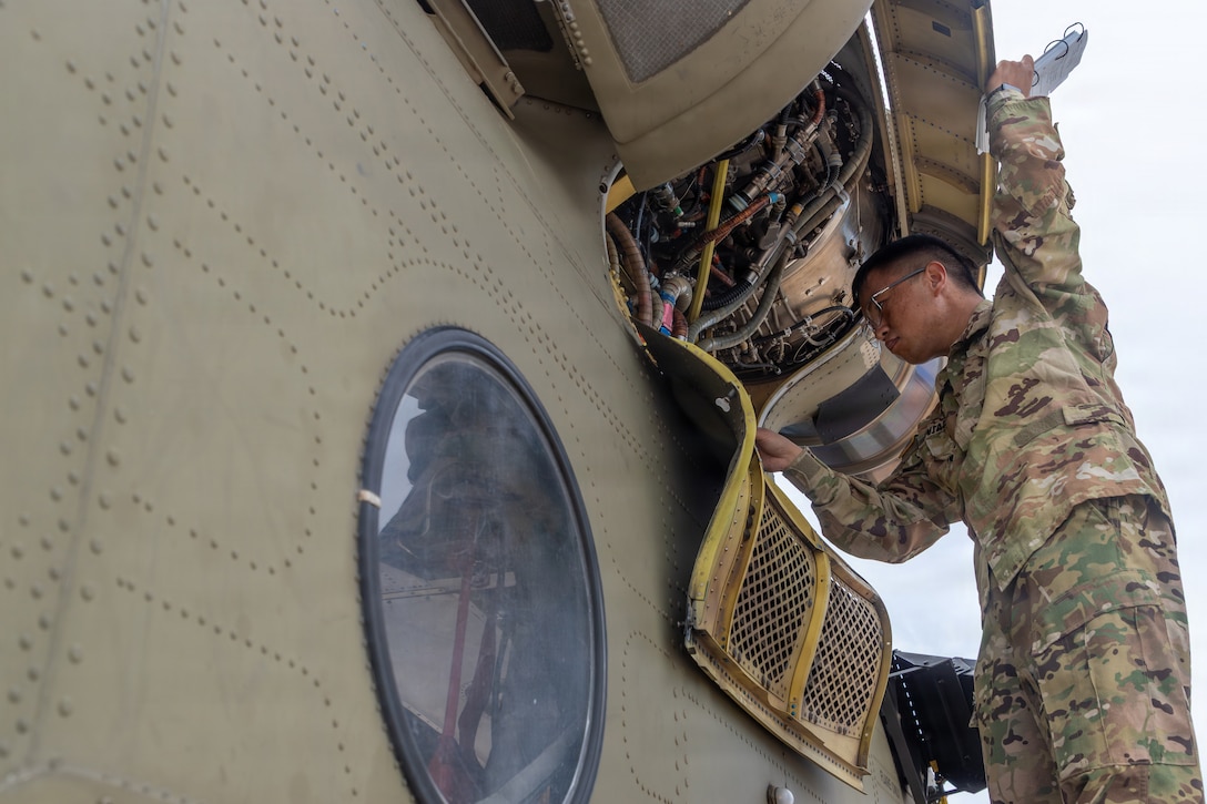 A soldier in camouflage uniform examines the engine on a helicopter outdoors.