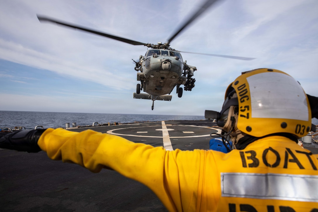 A U.S. Sailor signals to a MH-60S Sea Hawk helicopter, attached to Helicopter Sea Combat Squadron (HSC) 14 on the flight deck of the Arleigh Burke-class guided-missile destroyer USS Mitscher (DDG 57), April 15, 2026. Mitscher is deployed to the U.S. 5th Fleet area of operations to support maritime security and stability in the Middle East. (U.S. Navy photo)