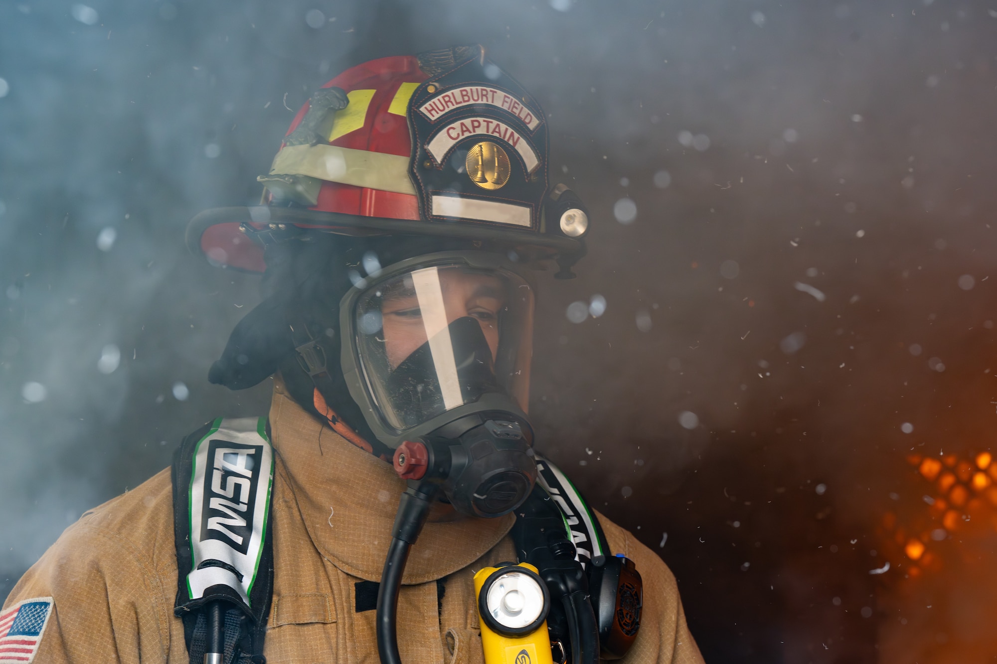 A firefighter exits a burning building surrounded by smoke and flames.