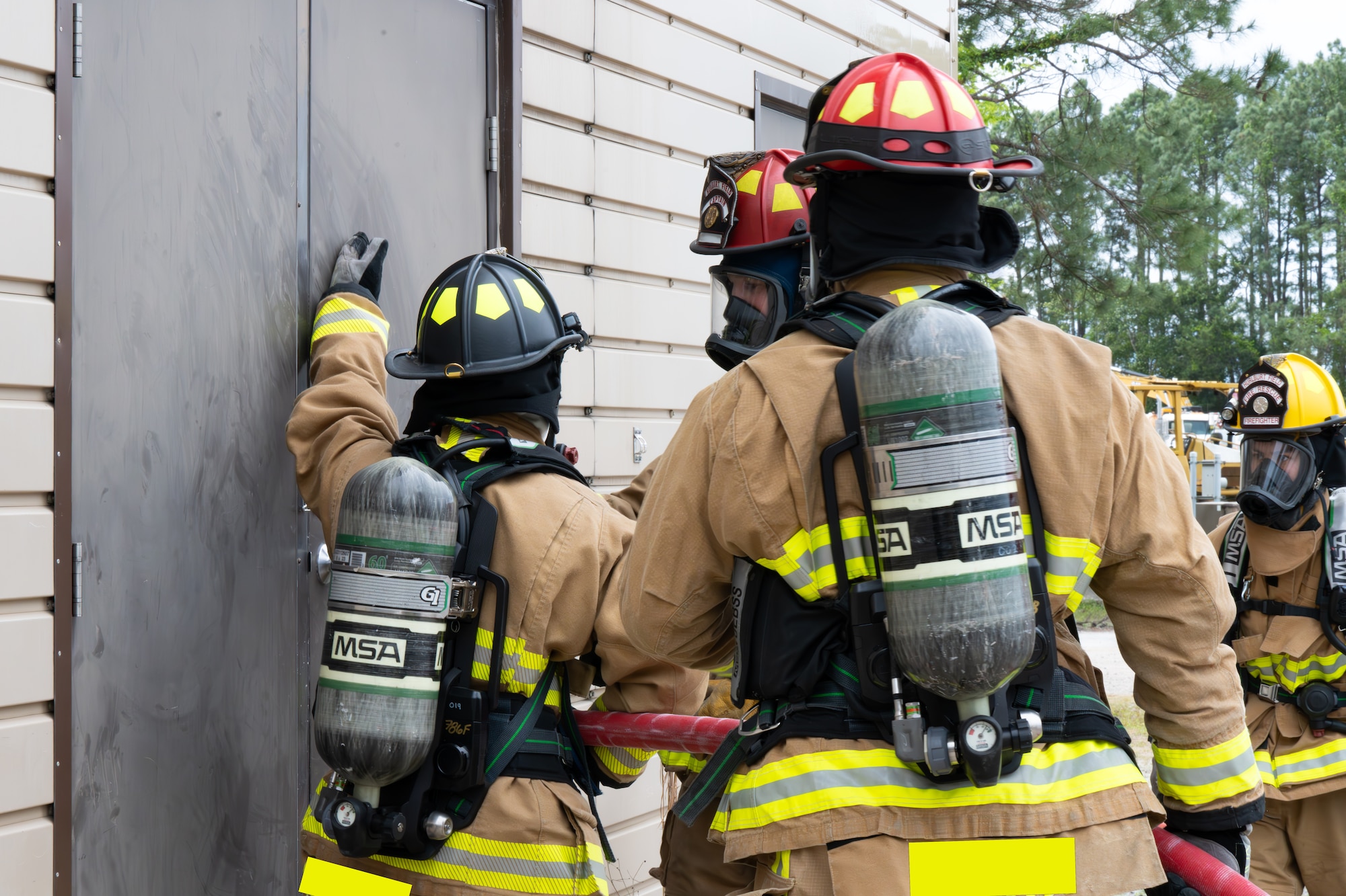 Firefighters in full gear feel a door for heat while preparing to enter a building.