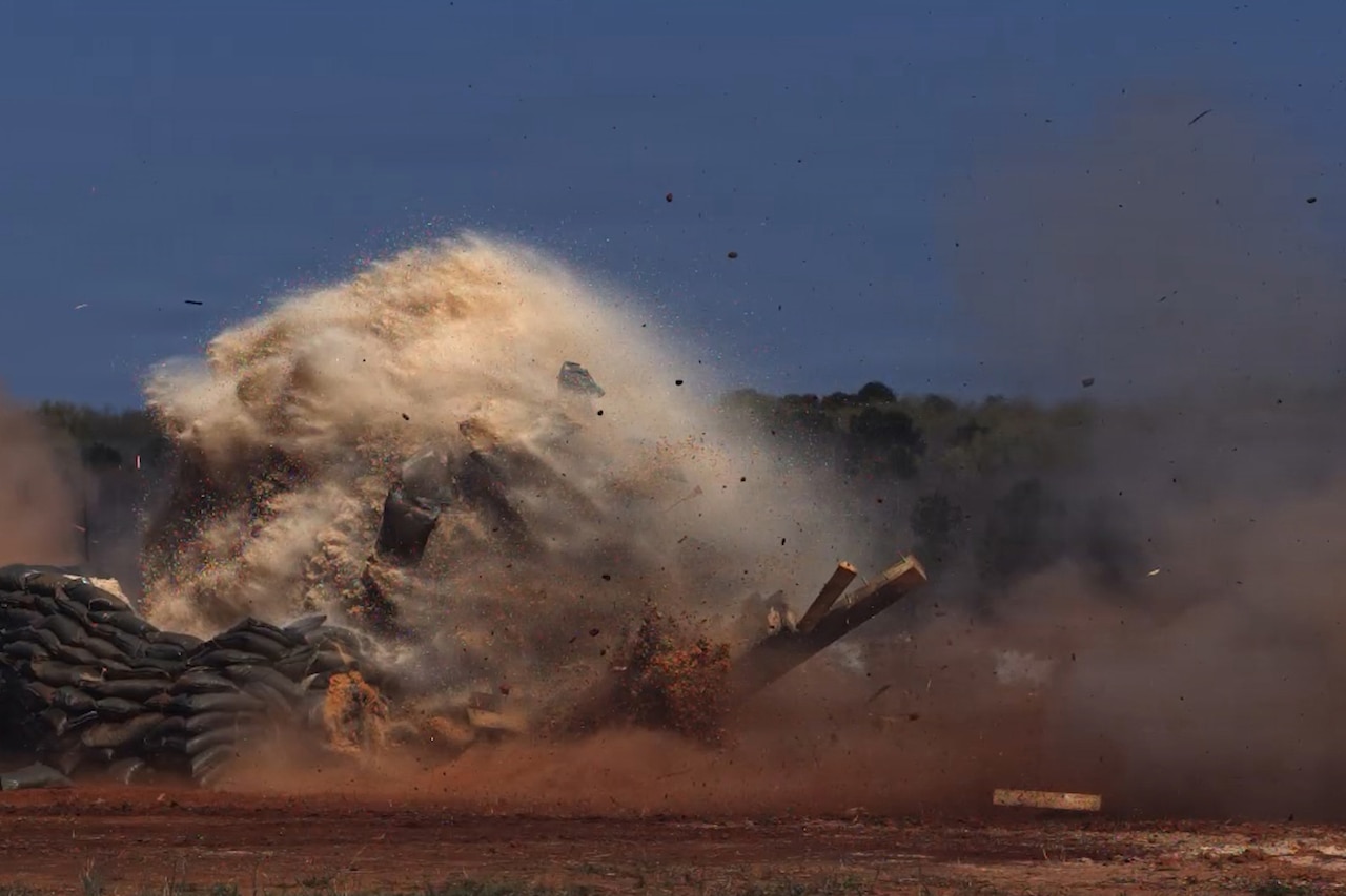 A large, clouded explosion of dust and debris fills the sky as it rises from the ground.