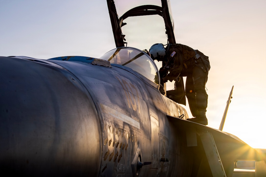 A pilot steps into the cockpit of a fighter jet.
