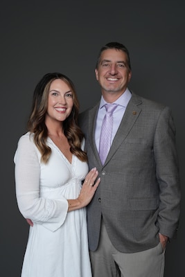 An image of a man and woman. The woman is wearing a white dress, and the man is wearing a gray suit.