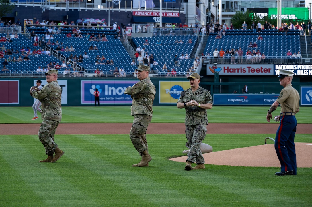 4 military leaders throw a pitch on the field.